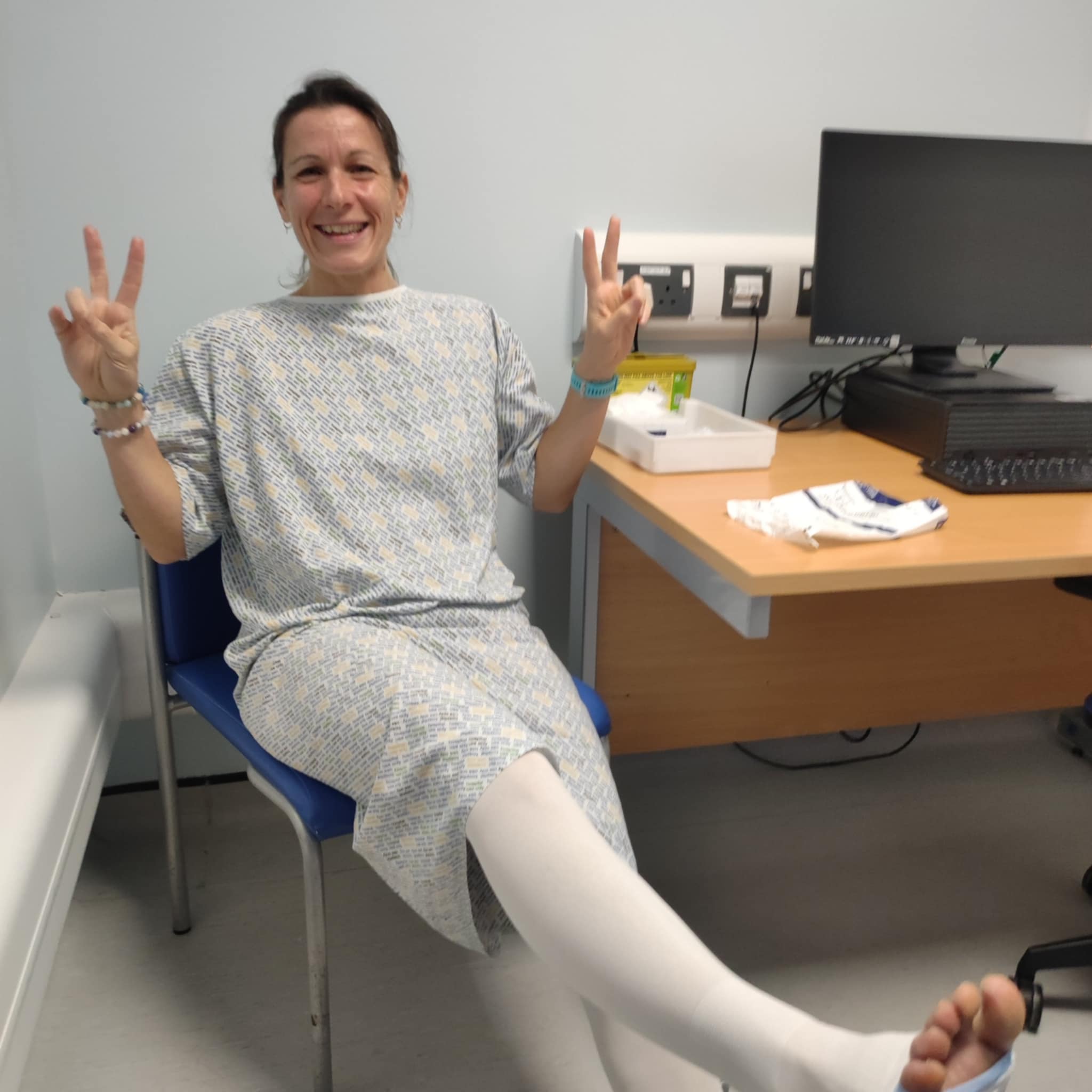 Lisa in hospital gown before surgery, giving peace signs with a smile
